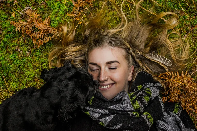 Mujer abrazando a un perro negro entre hojas de otoño